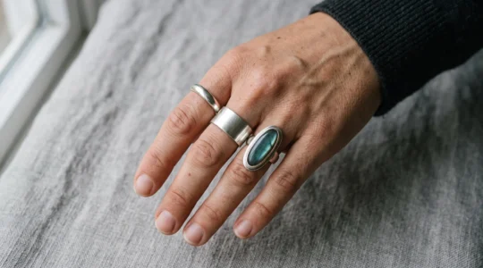 A woman's hand wearing three different silver ring styles, comparing band widths and stone shapes under natural light.